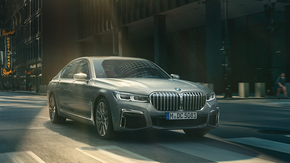 Driving Assistant Professional: three-quarter front view of BMW 7 Series Sedan driving in front of urban setting Driving Assistant Professional: three-quarter front view of BMW 7 Series Sedan driving in front of urban setting