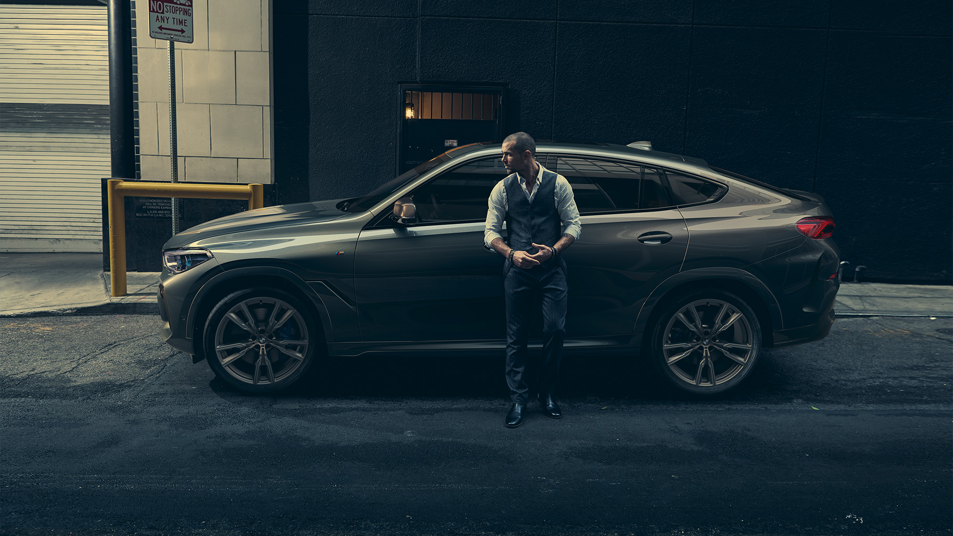 BMW X6 M50i in lateral perspective Man leaning on BMW X6 M50i in lateral perspective in front of an urban setting