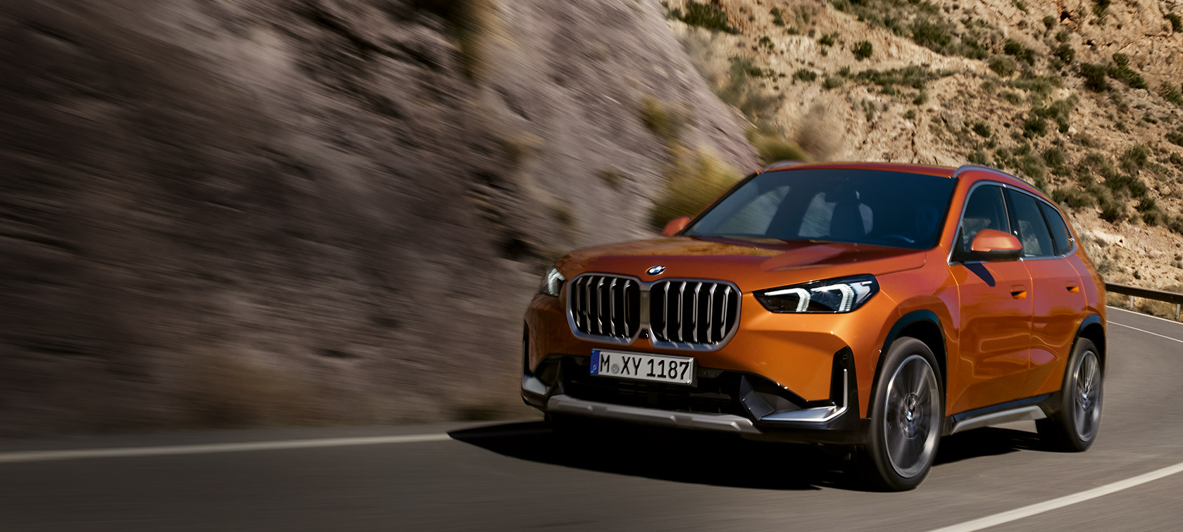 BMW X1 U11 xLine Utah orange metallic three quarter front view BMW X1 U11 xLine Utah orange metallic three quarter front view driving on country road